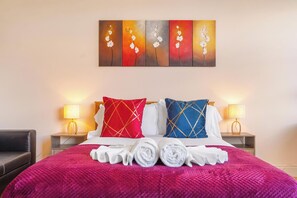 A hotel room with a bed, two nightstands, a lamp, and a painting above the bed. - Bright 1BR Apartment in Shoreditch Brick Lane Close to Tube Sleeps 4 (London)