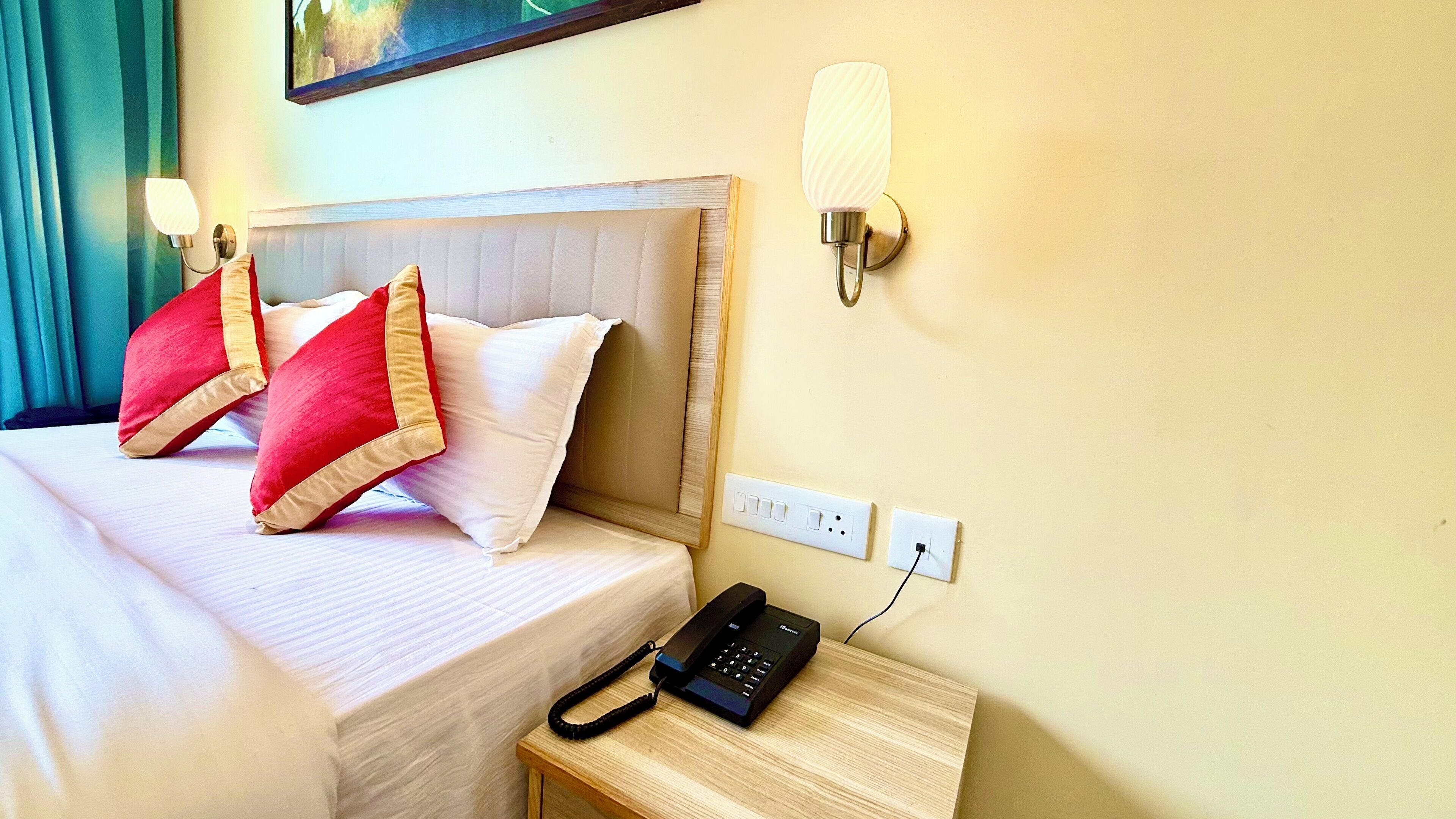 A hotel room with a bed, two pillows, a bedside table with a phone, and wall-mounted lights.