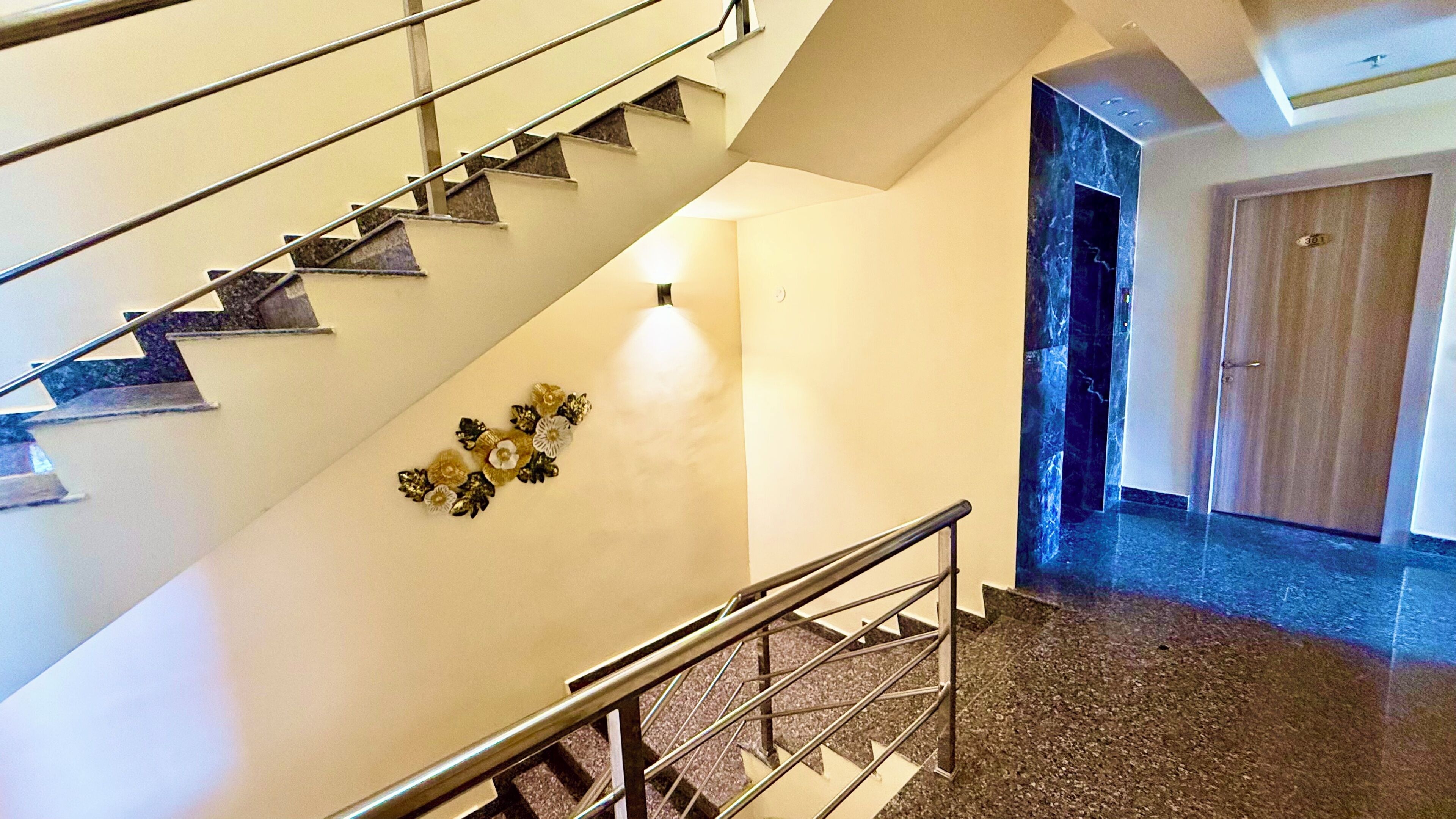 A staircase with metal railings, a wall-mounted decorative floral arrangement, and a door with a number sign.