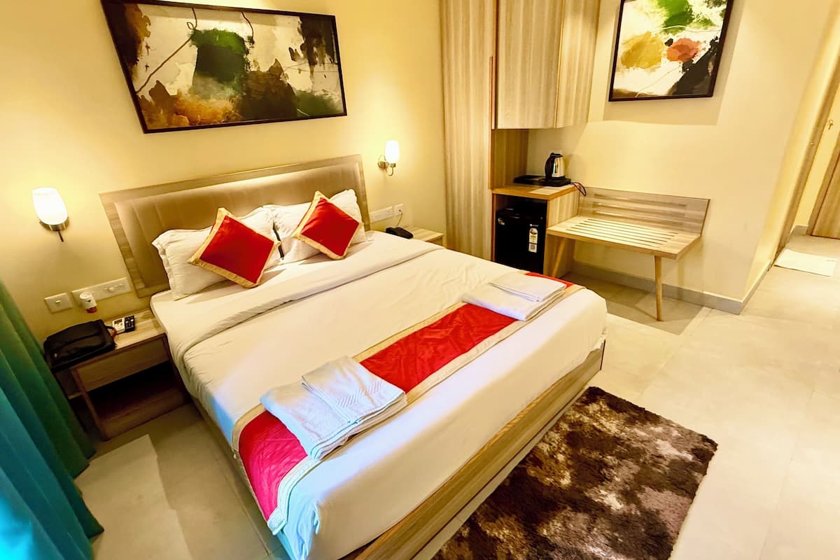 Una habitación de hotel con una cama grande, una mesita de noche, un banco y obras de arte en las paredes.