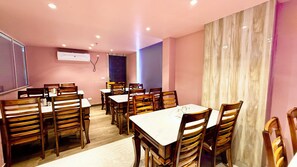Un espace repas avec des chaises et des tables en bois, un tableau blanc accroché au mur et une fenêtre avec des rideaux.