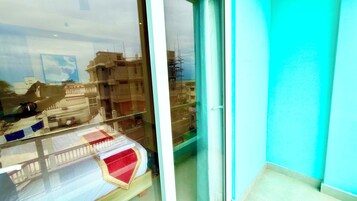 Una habitación con vistas a un paisaje urbano a través de una ventana, una cama con colcha roja y blanca, y una pared azul.