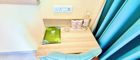 Une petite table en bois, un menu vert, une bougie dans un verre, une bouteille d’eau et une paire de chaussons.