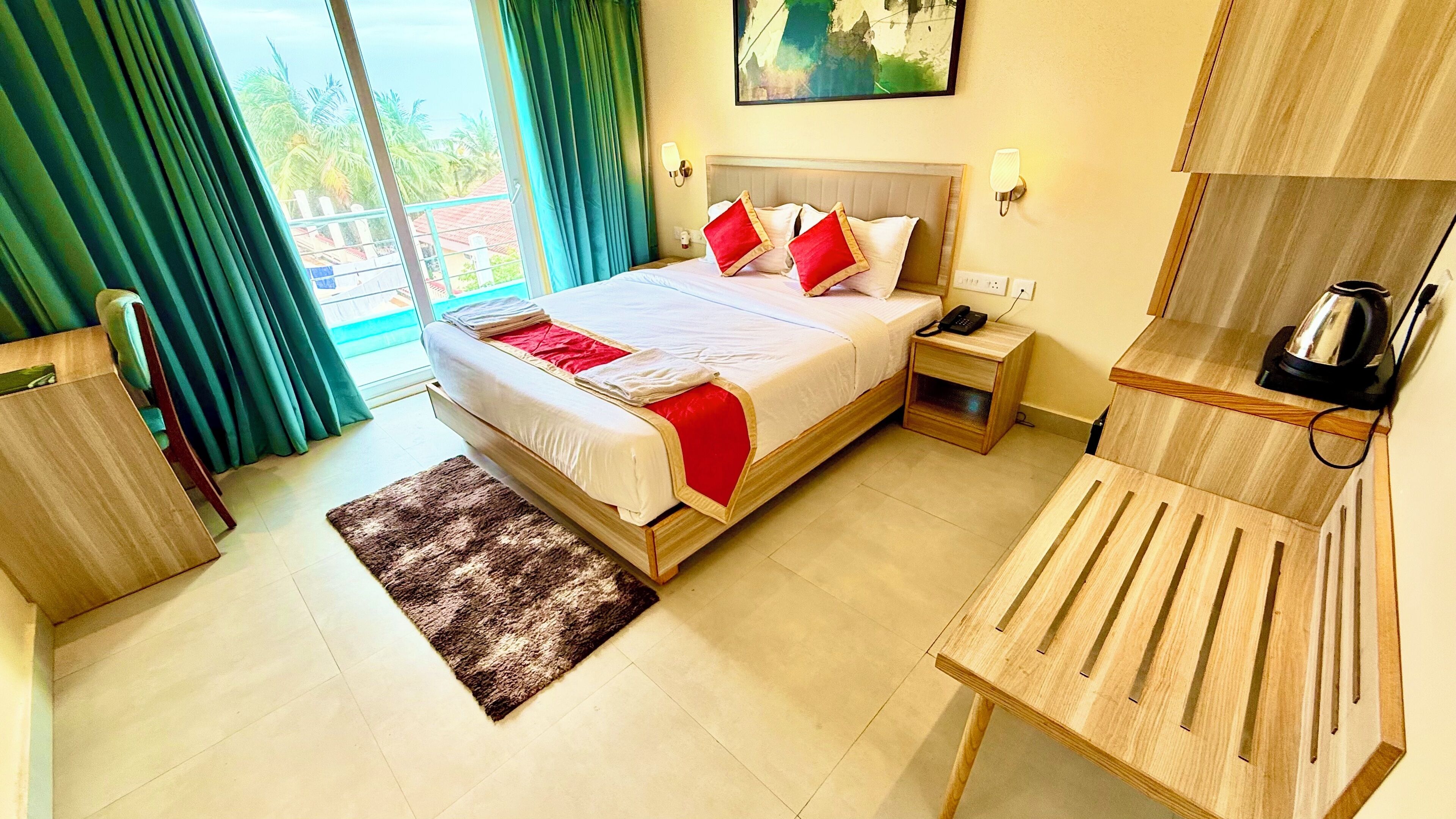 Hotelkamer met een bed, nachtkastje, klein houten nachtkastje, bureau, stoel, raam met gordijnen en een schilderij aan de muur.