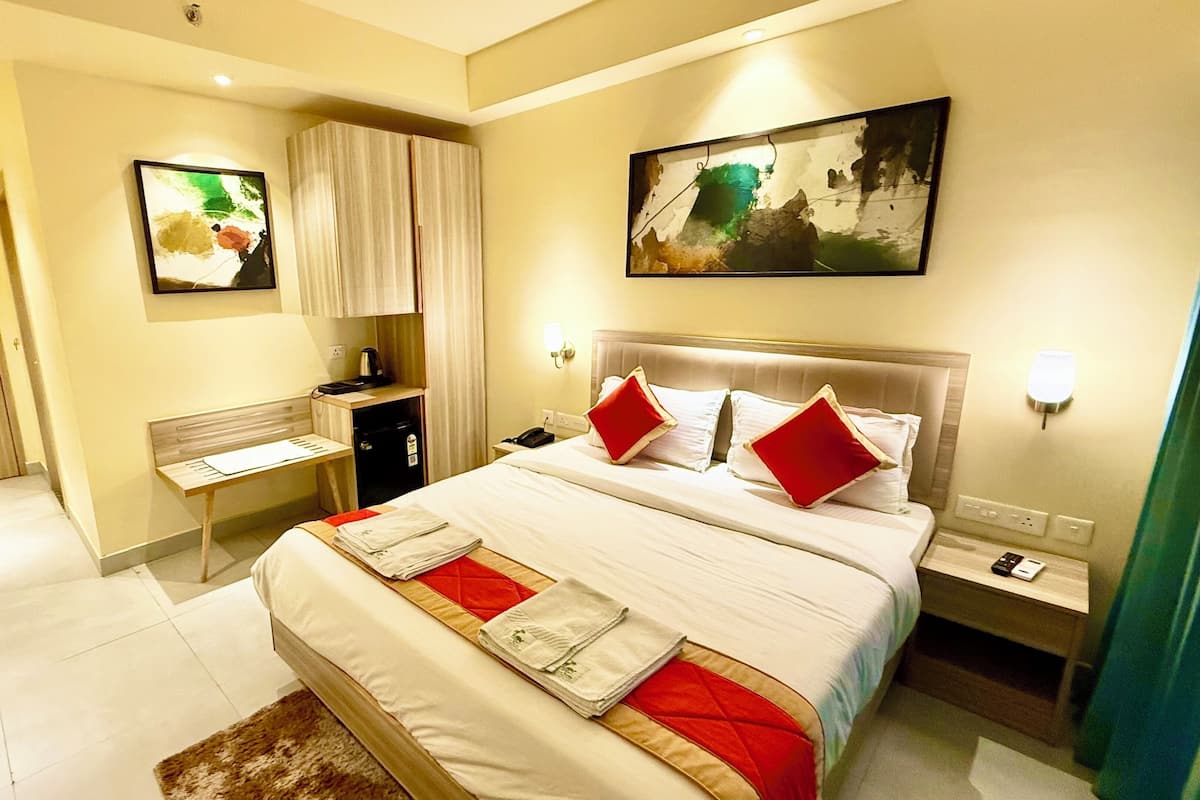 Habitación de hotel con cama, escritorio, silla, mesita de noche, un cuadro y una puerta.