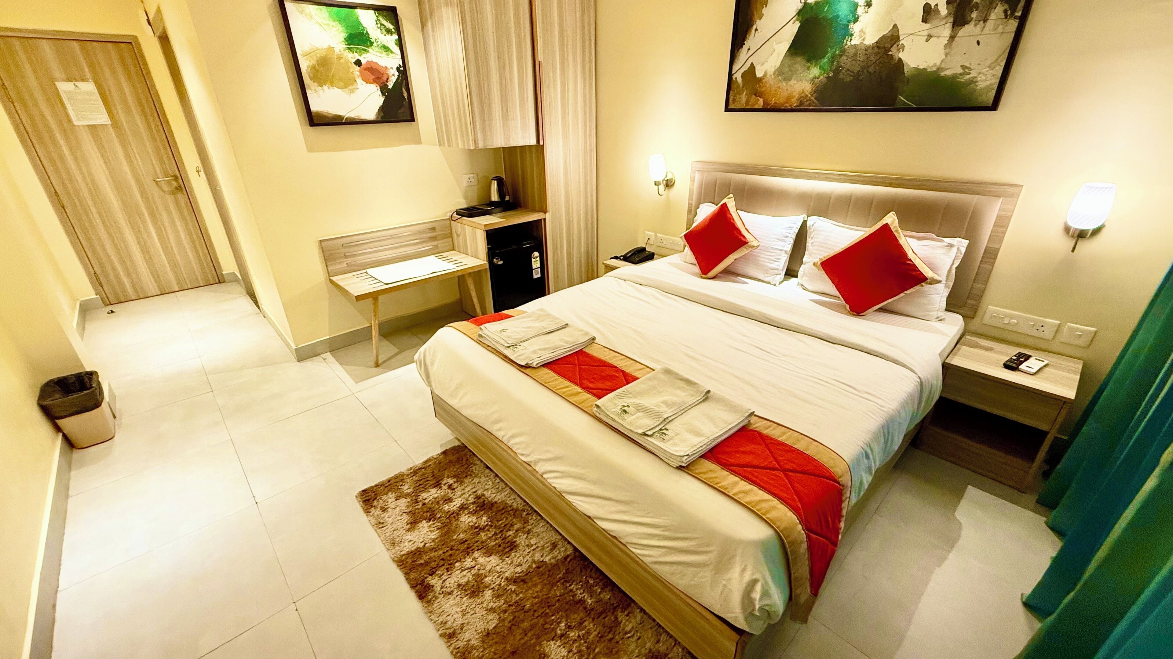 Une chambre d’hôtel avec un grand lit, une table de chevet, une commode, un bureau, une poubelle et une porte.