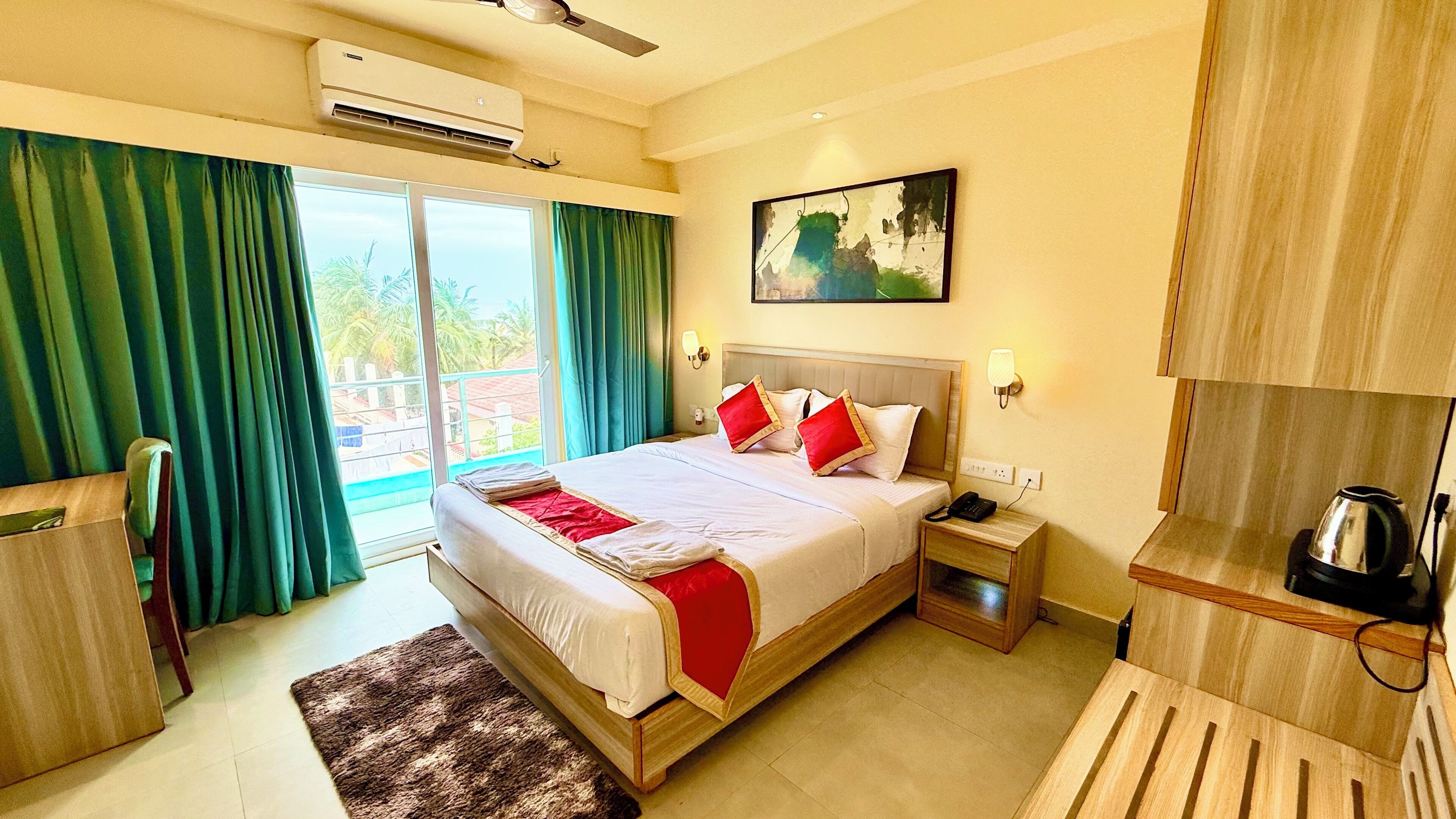 A hotel room with a bed, a bedside table with a phone, a kettle, and a view of the outdoors.