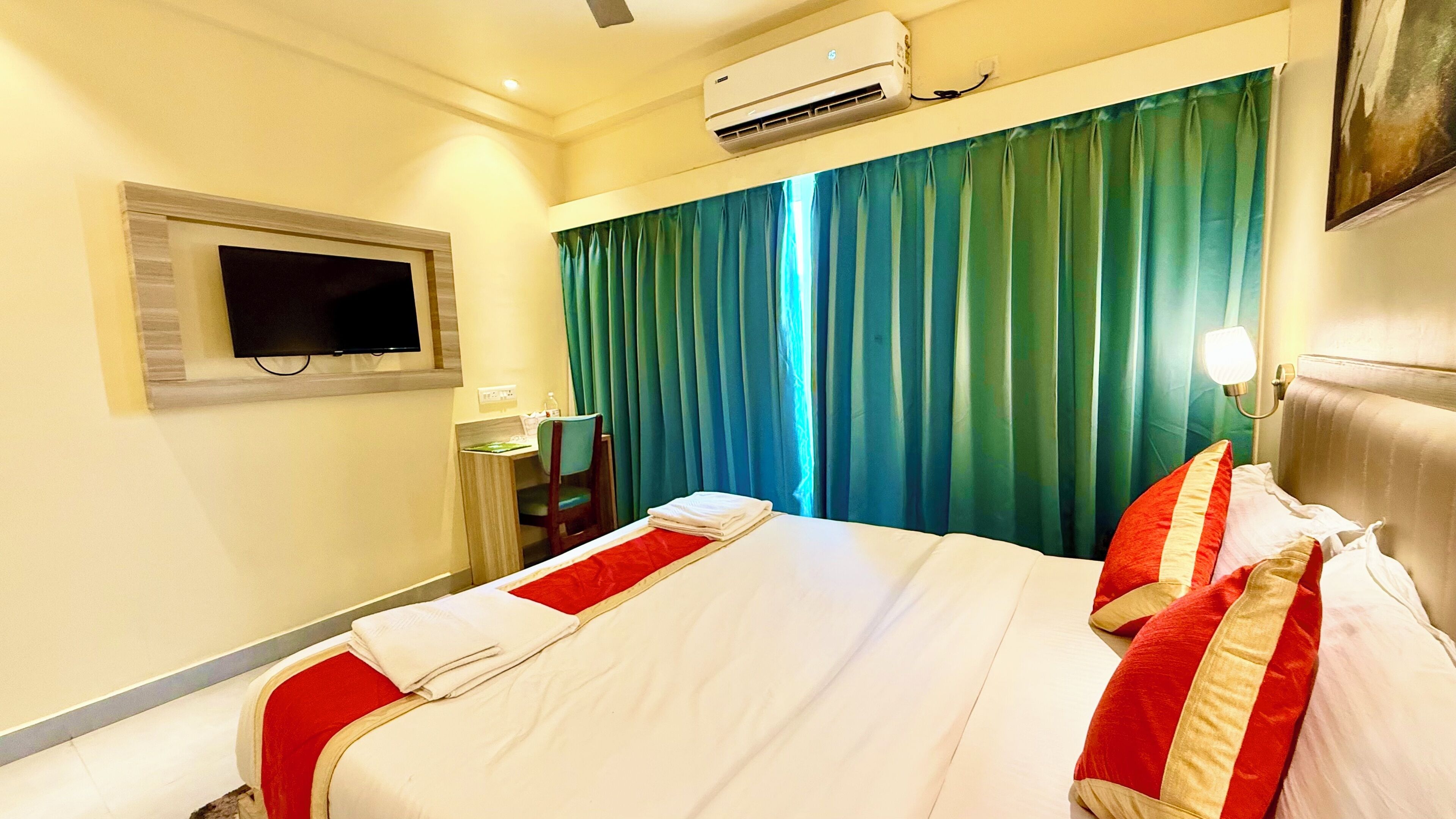 A hotel room with a bed, a desk, a chair, a television, and a window with curtains.