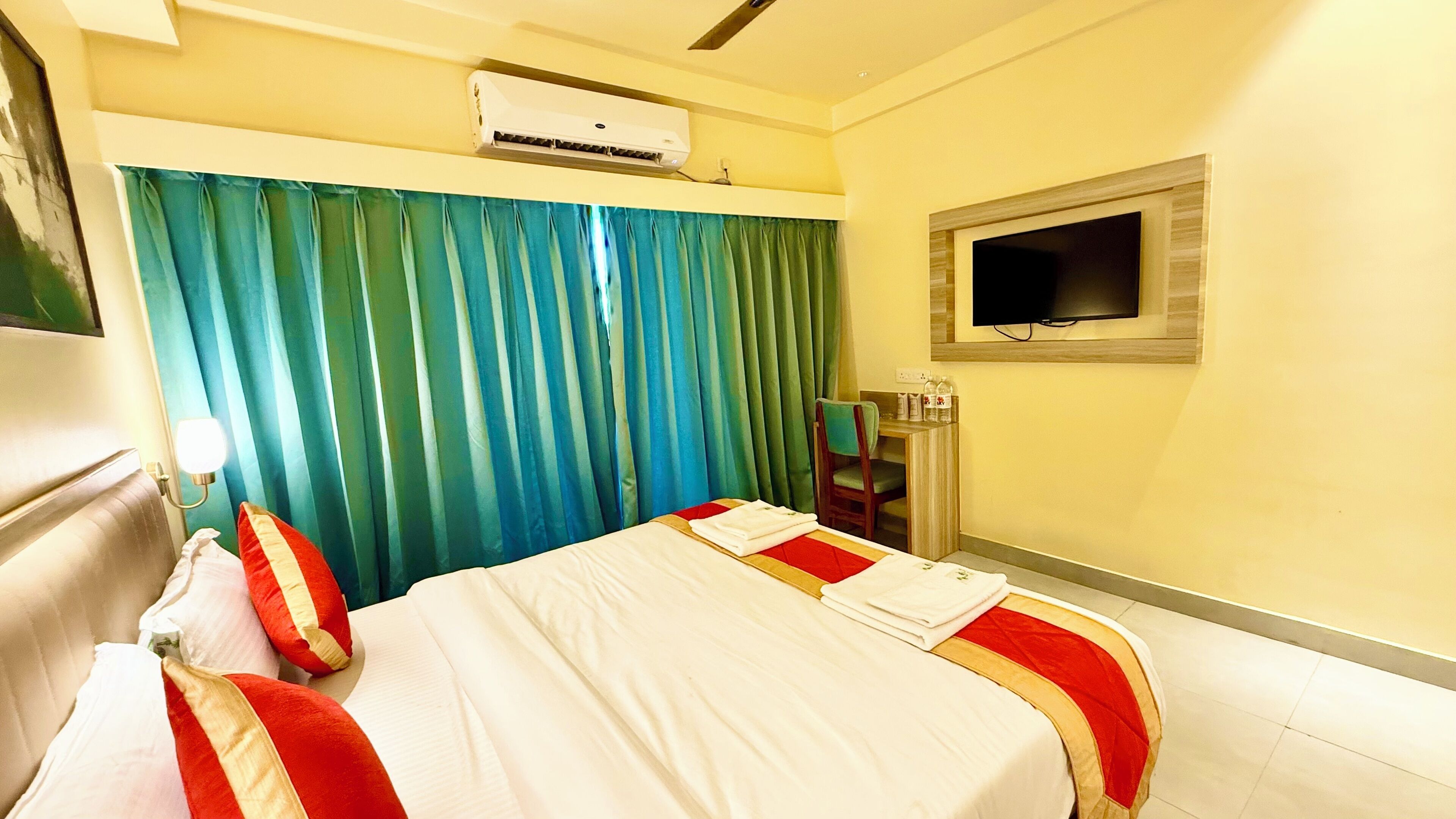 A hotel room with a bed, a TV mounted on the wall, and a window with curtains.
