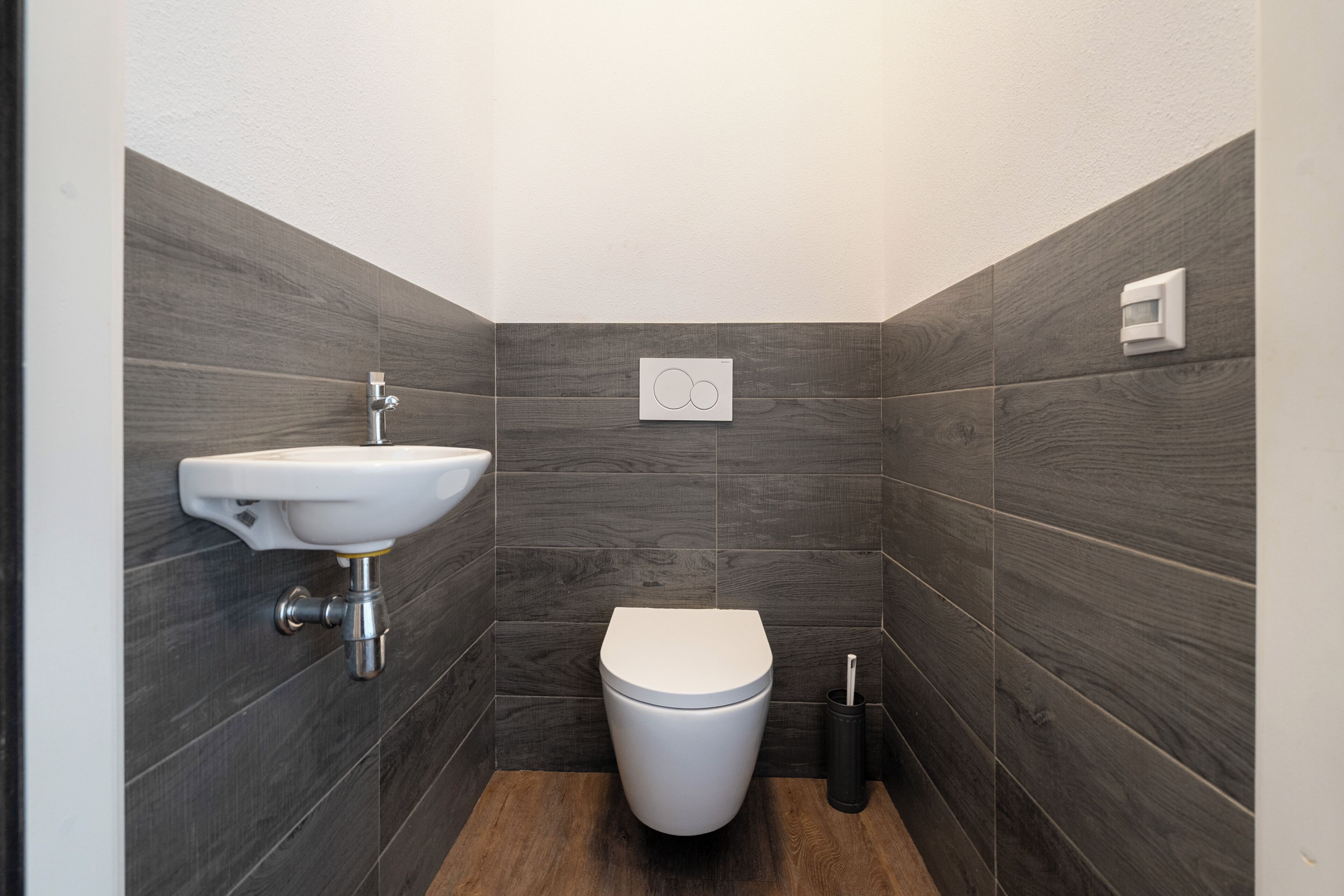A modern bathroom with a white sink, toilet, and dark wood-patterned walls.