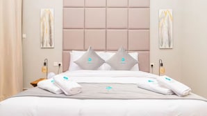 Una cama bien hecha con cabecera acolchada, dos almohadas y un juego de toallas dobladas.