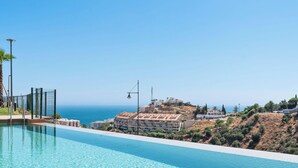 En swimmingpool med utsikt över havet och byggnader i bakgrunden.