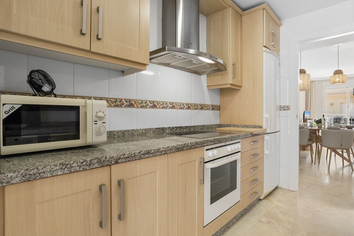 A kitchen with wooden cabinets, a microwave, an oven, and a fan.