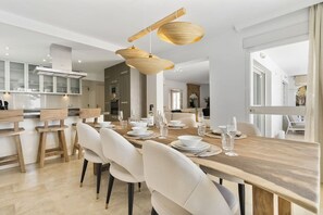 A modern dining area with a wooden table set for six, white chairs, and a hanging light fixture. - Villa Torre Alta | Views - Pool - Terrace (Mijas Costa)