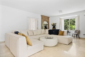 A modern living room with a beige sectional sofa, a round coffee table, and a large mirror. - Villa Torre Alta | Views - Pool - Terrace (Mijas Costa)