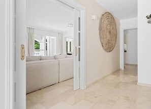 A hallway with a beige wall, a textured artwork, and a white door leading to a room with a beige sofa. - Villa Torre Alta | Views - Pool - Terrace (Mijas Costa)