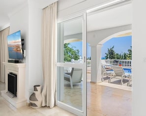 A hotel room with a TV, a fireplace, a large sliding glass door leading to a balcony with outdoor furniture. - Villa Torre Alta | Views - Pool - Terrace (Mijas Costa)