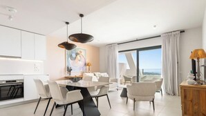 Moderni hotellihuone, jossa on ruokailutila, keittiö ja suuret ikkunat, joista on näkymä.