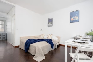 Un dormitorio con una cama, una mesita de noche con vasos, un cuadro en la pared y una puerta que da a otra habitación.