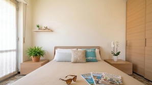 Un dormitorio con cama, mesitas de noche, una estantería con objetos decorativos y una ventana con cortinas.
