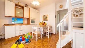 Una cocina con televisión, cesta de frutas y una mesa de comedor con sillas.