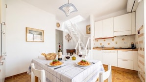 Un comedor con una mesa lista para dos, una cocina con armarios blancos y una escalera que lleva a otro nivel.