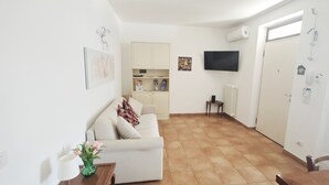 A compact living space with a sofa, a dining table, a small kitchen area, and a TV mounted on the wall. - Relaxation in Holiday House Calmasino (Veneto)