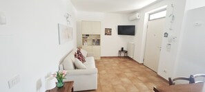 A compact living space with a sofa, a dining table, a small kitchen area, and a TV mounted on the wall. - Relaxation in Holiday House Calmasino (Veneto)