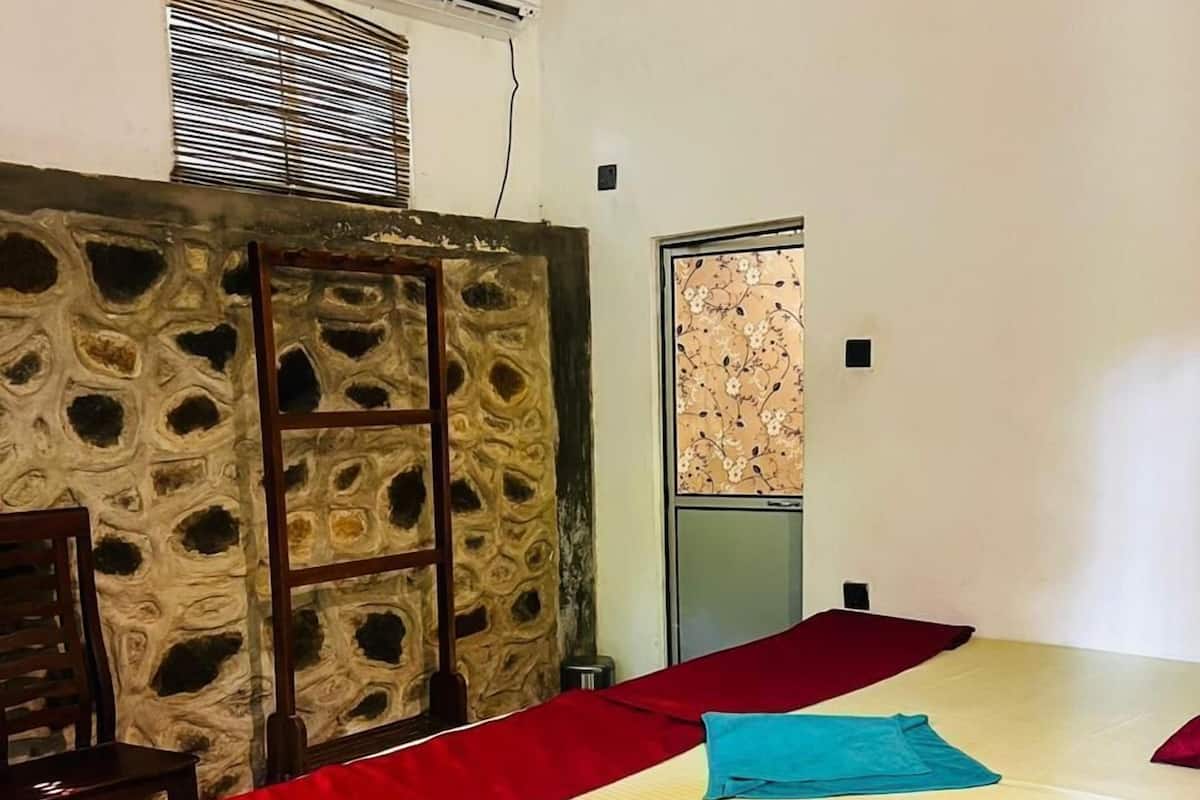 Ein Zimmer mit einem Bett, einem Holzstuhl, einer Steinwand und einer Klimaanlage.