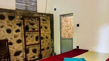 A room with a bed, a wooden chair, a stone wall, and an air conditioning unit.