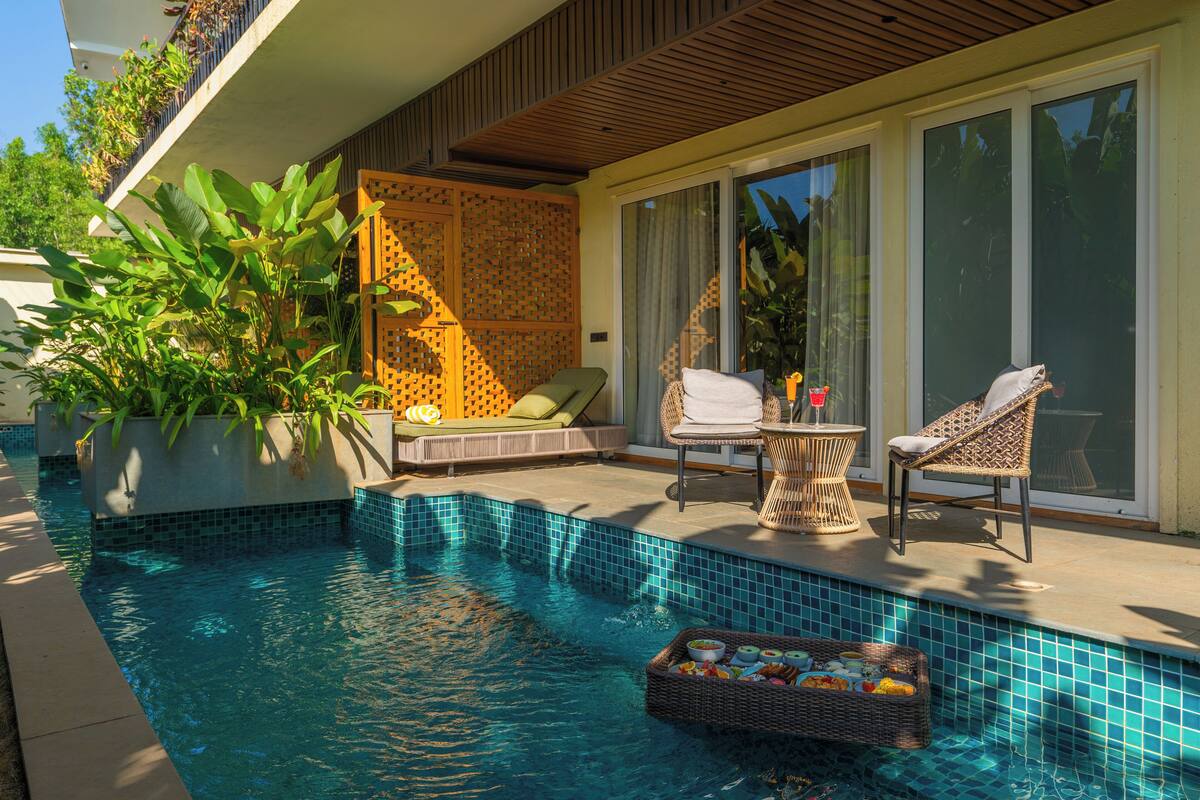 Una piscina con borde de azulejos, una cesta de mimbre con aperitivos y dos sillones de mimbre.