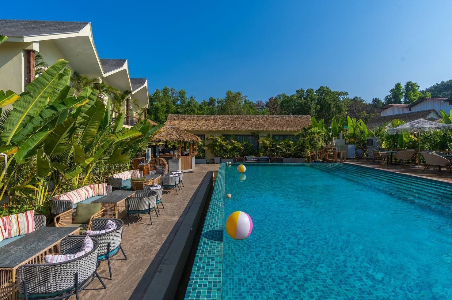 A poolside area with lounge chairs and a bar, surrounded by tropical plants and a clear blue pool.