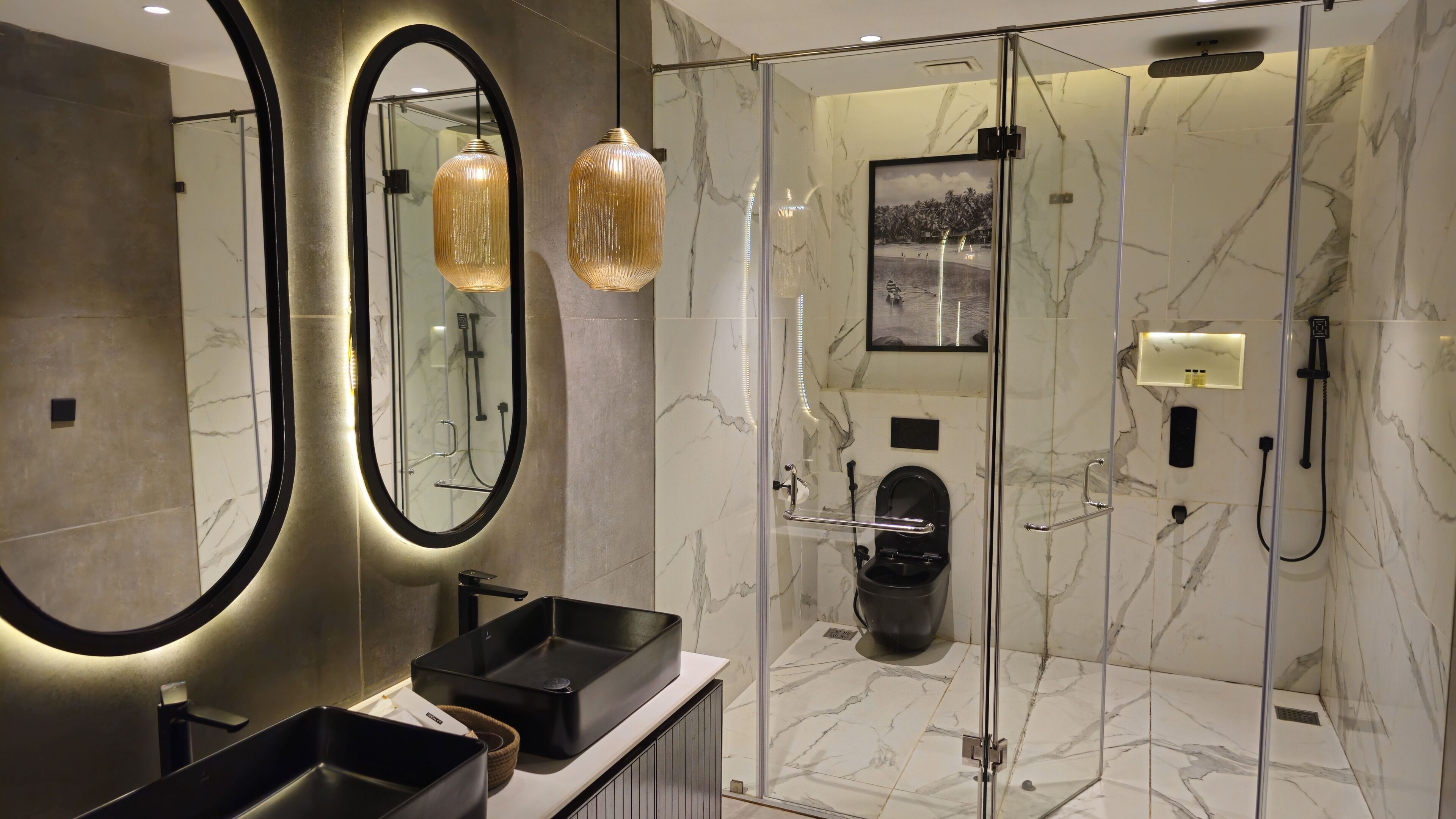 A modern bathroom with a large mirror, two black sinks, a glass-enclosed shower, and marble walls.