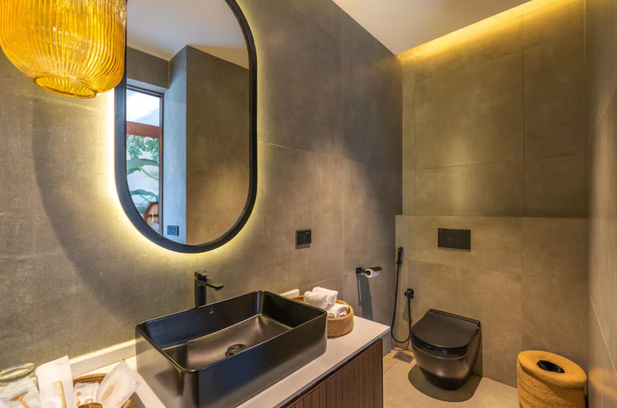 A modern bathroom with a large rectangular sink, a round mirror, and a shower area.