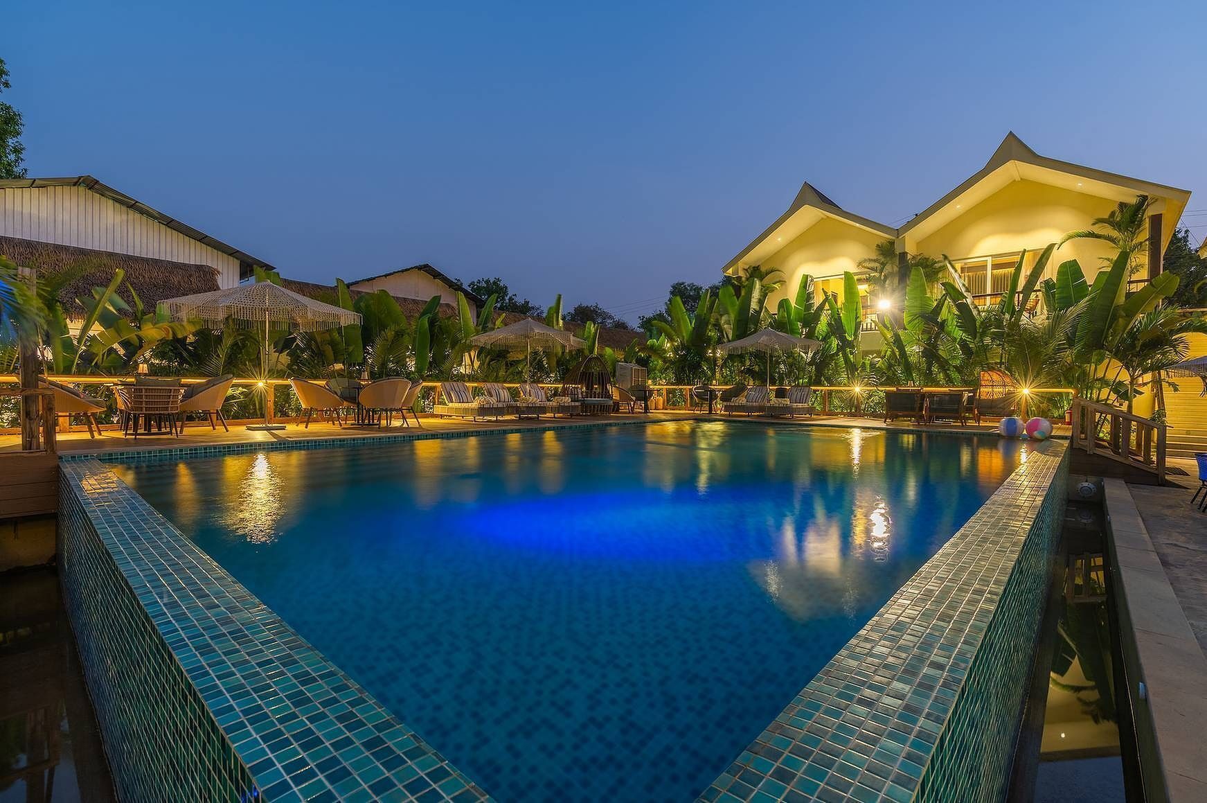 A swimming pool with lounge chairs and umbrellas, surrounded by buildings and palm trees.