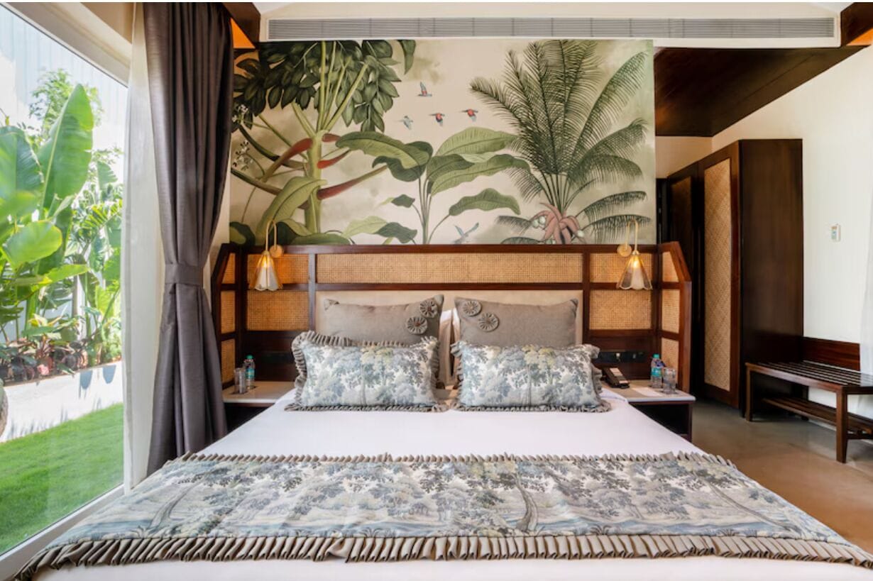 Ein Schlafzimmer mit einem großen Bett, einer Wandmalerei mit tropischen Pflanzen, einem Nachttisch und einer Bank.