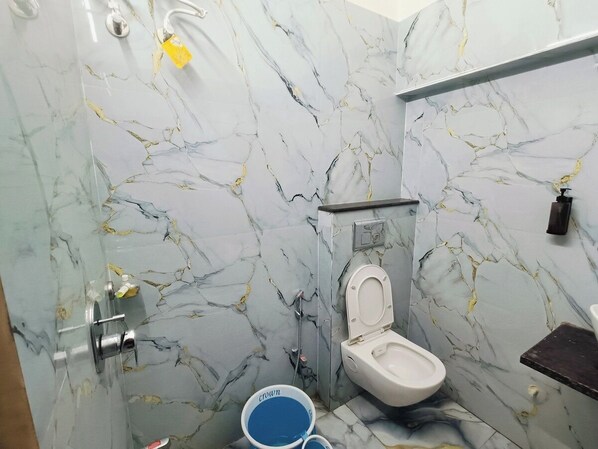 Une salle de bain avec des toilettes, une douche et un seau bleu.