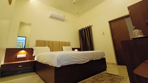 A hotel room with a bed, bedside table, nightstand, and an air conditioning unit. - Shree Gangesh Inn (Varanasi)