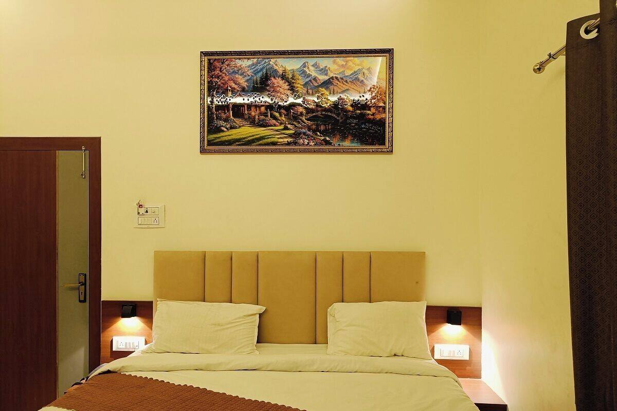 A hotel room with a bed, two bedside lamps, a wall-mounted painting, and a door.