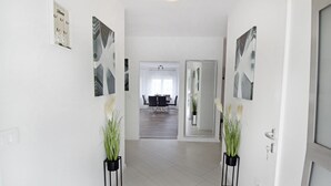 Ein Flur mit zwei Kübelpflanzen, ein Essbereich mit Tisch und Stühlen und ein großer Spiegel an der Wand.