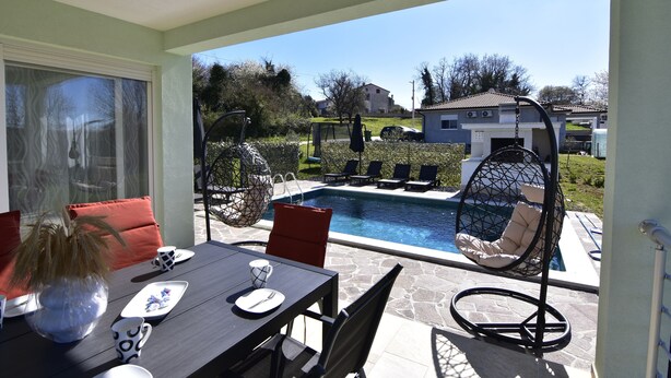 Eine Terrasse mit Esstisch, Stühlen und einer Hängematte neben einem Swimmingpool.
