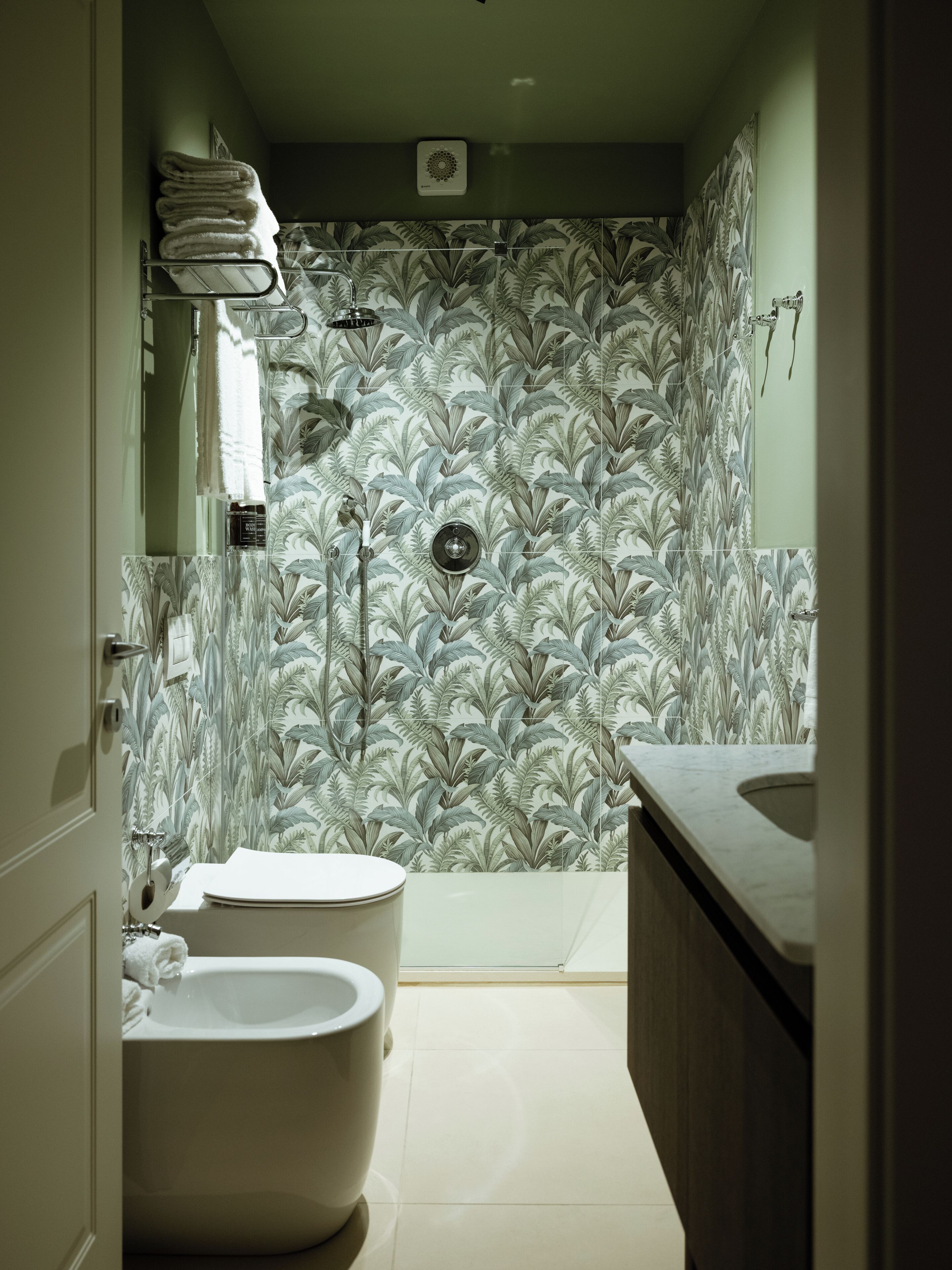 A bathroom with a toilet, bidet, and a shower with a leaf-patterned wall.