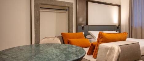 A hotel room with a bed, a sofa, a round table, and a door.