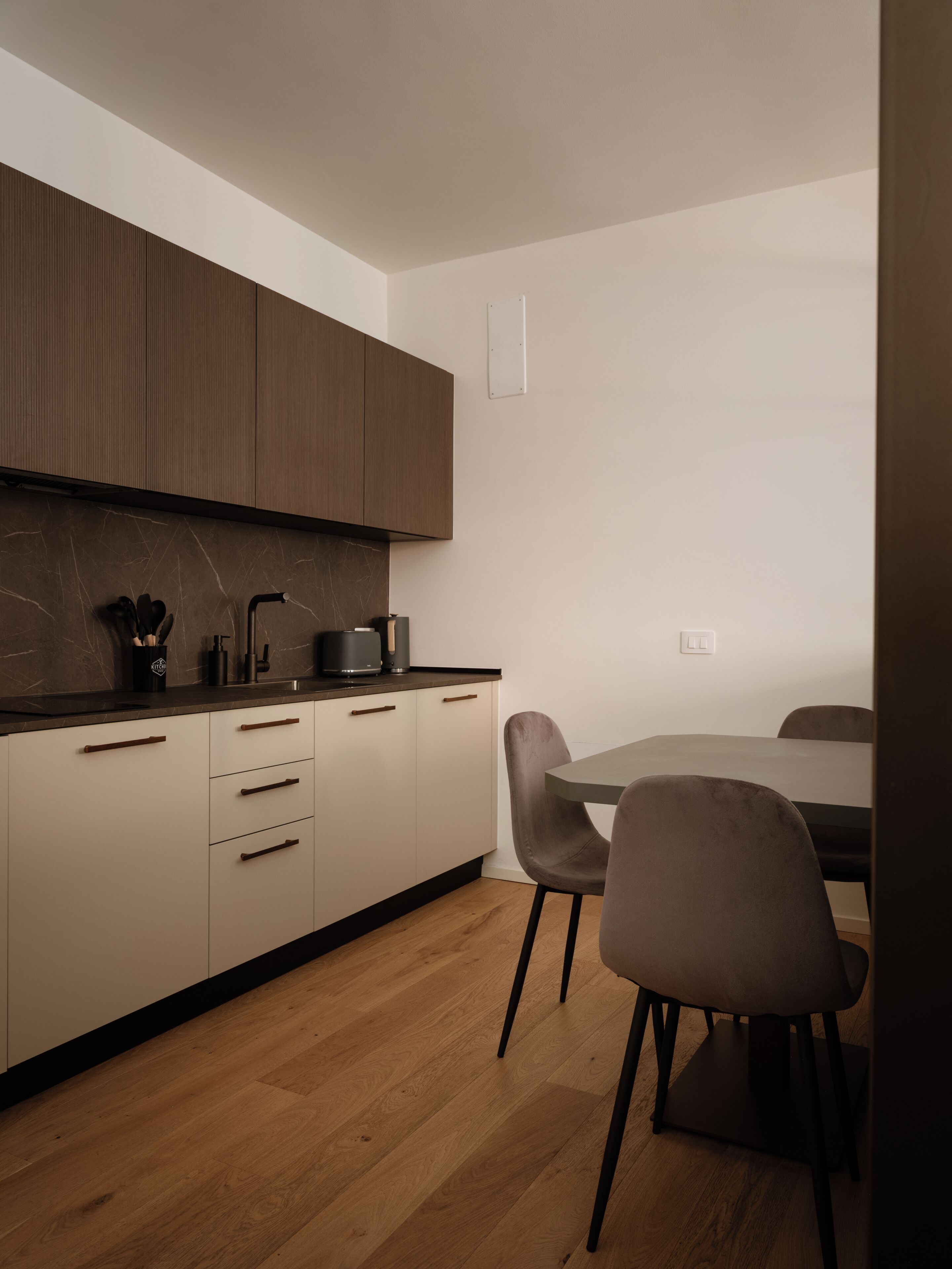 Een moderne keuken met houten kastjes, een marmeren aanrechtblad en een eethoek met tafel en stoelen.