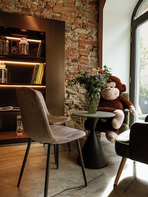 A cozy seating area with a plush chair, a small round table with a vase of flowers, and a large stuffed animal.