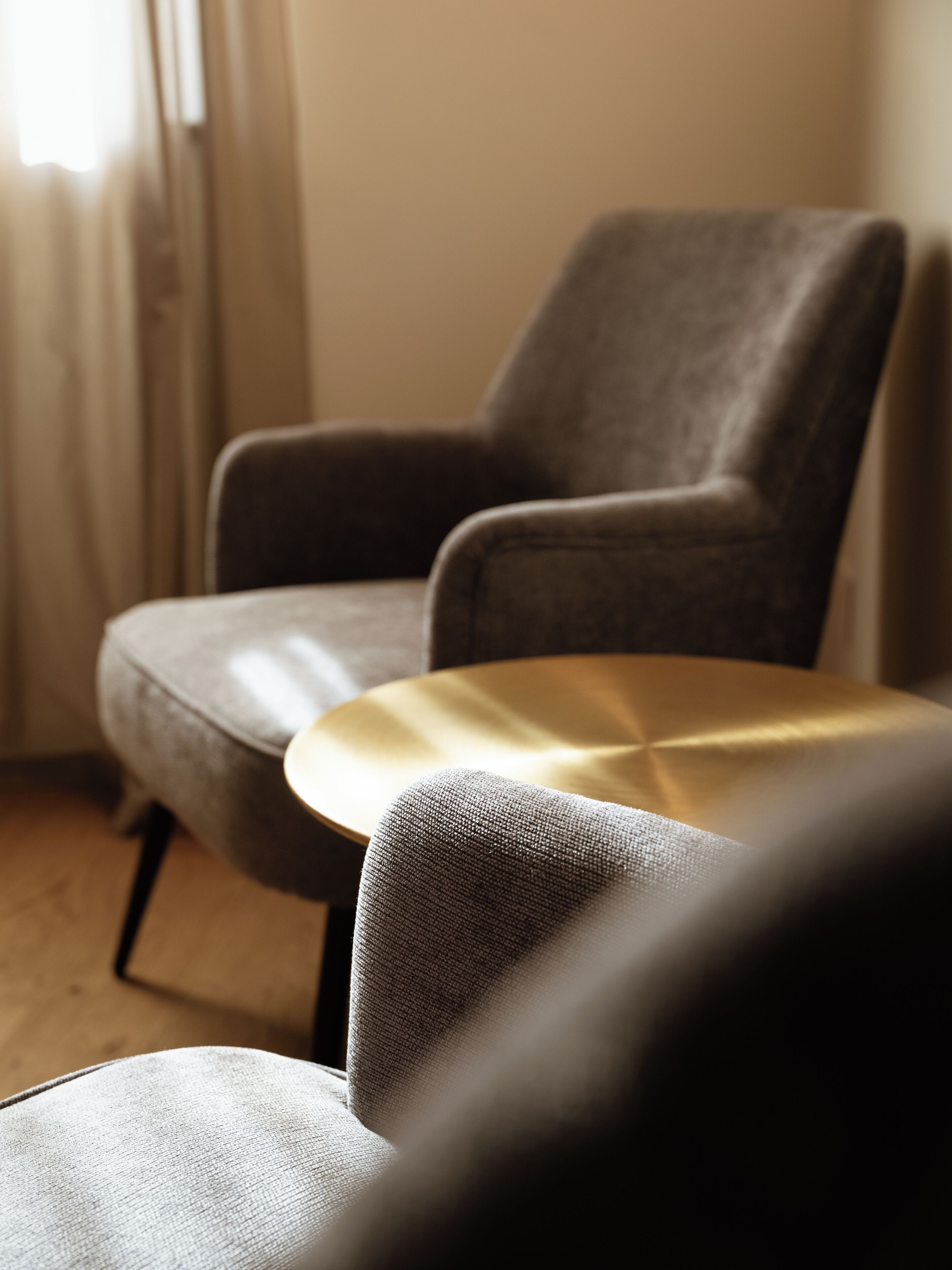 A chair and a small table in a room with a wooden floor and a window with curtains.
