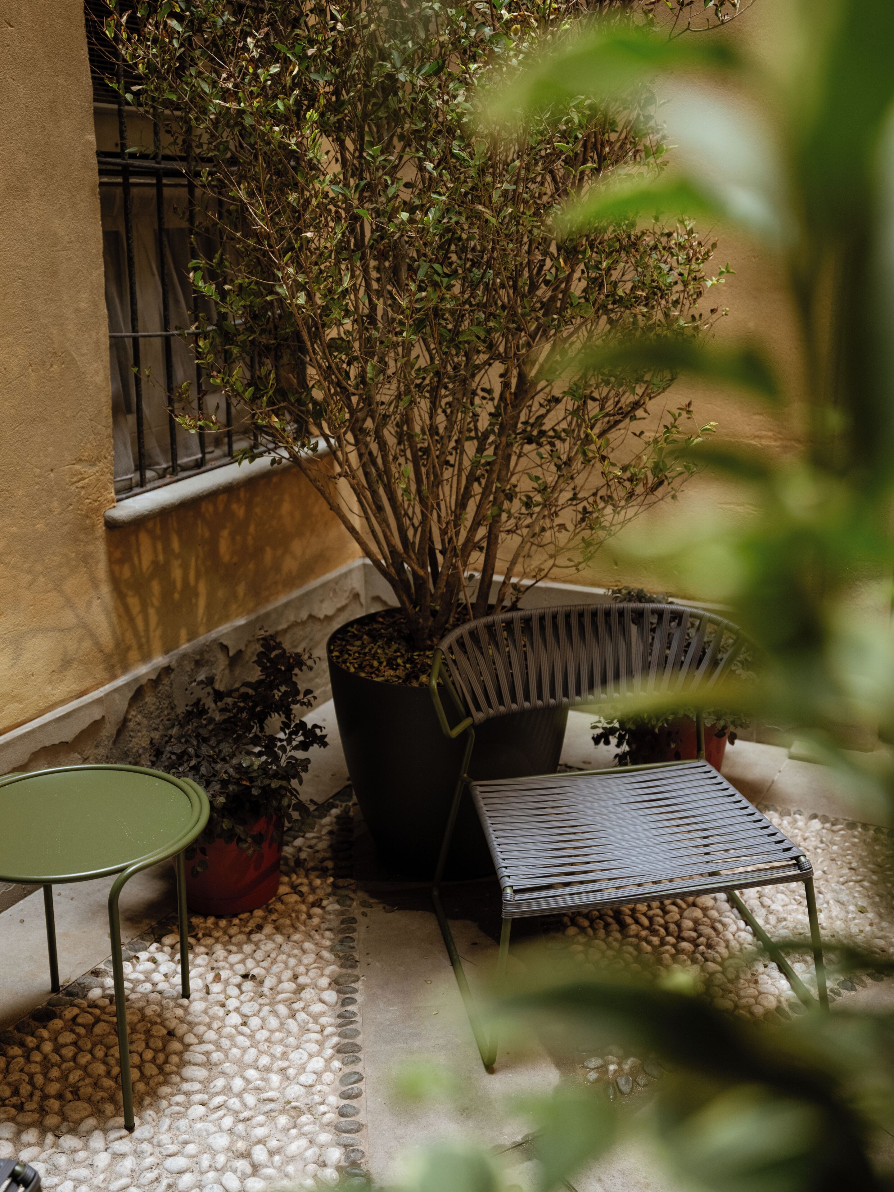 An outdoor seating area with a table and chairs, surrounded by potted plants and a small garden.