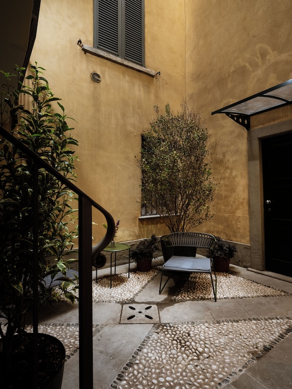 An outdoor seating area with a table and chairs, surrounded by potted plants and a gravel pathway.