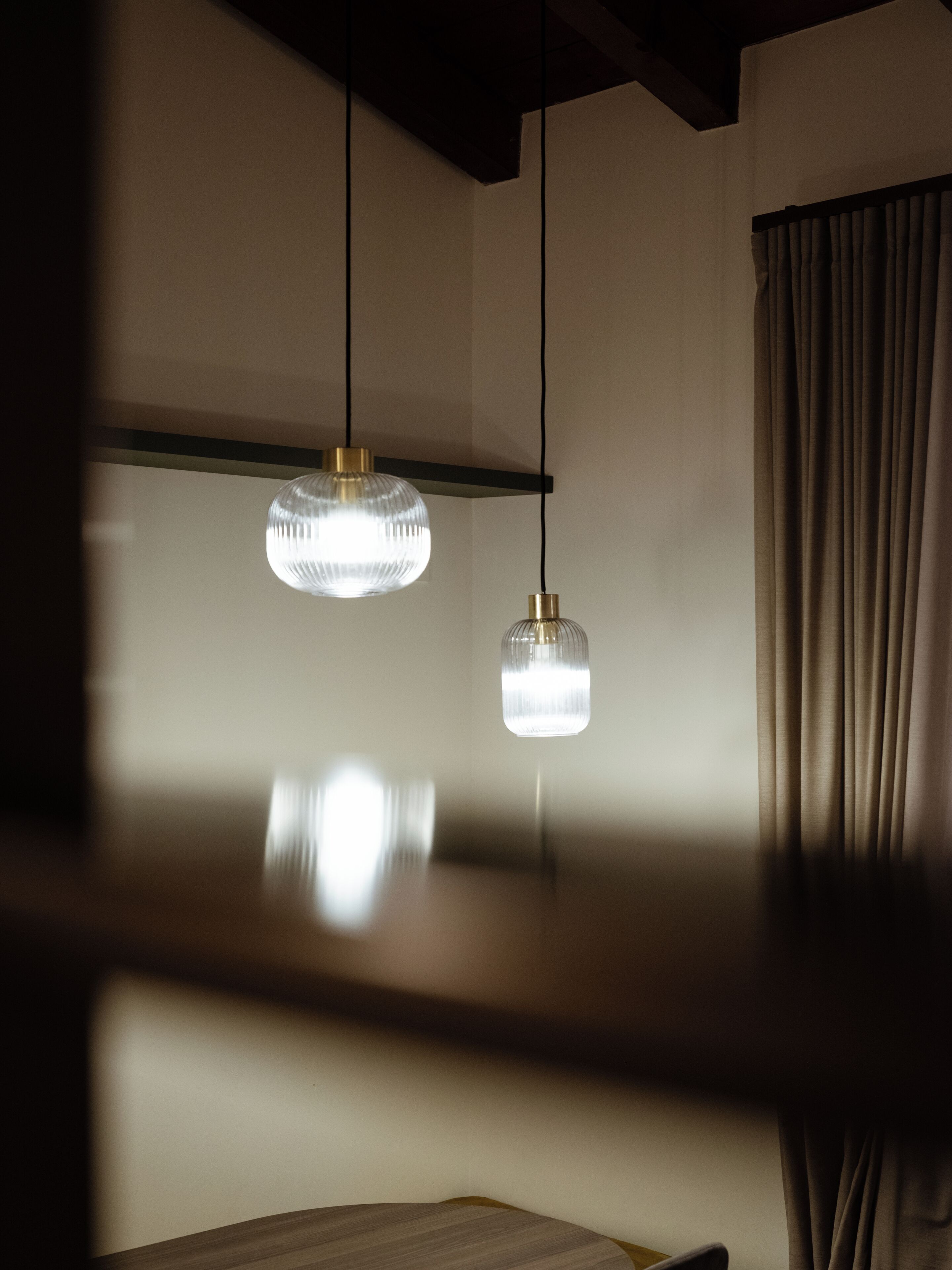 A room with a wooden ceiling, two hanging pendant lights, and a window with curtains.