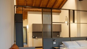 A modern hotel room with a wooden ceiling, a grey sofa, a bed, and a small kitchenette. - Ca Moroni Collection (Bergamo)